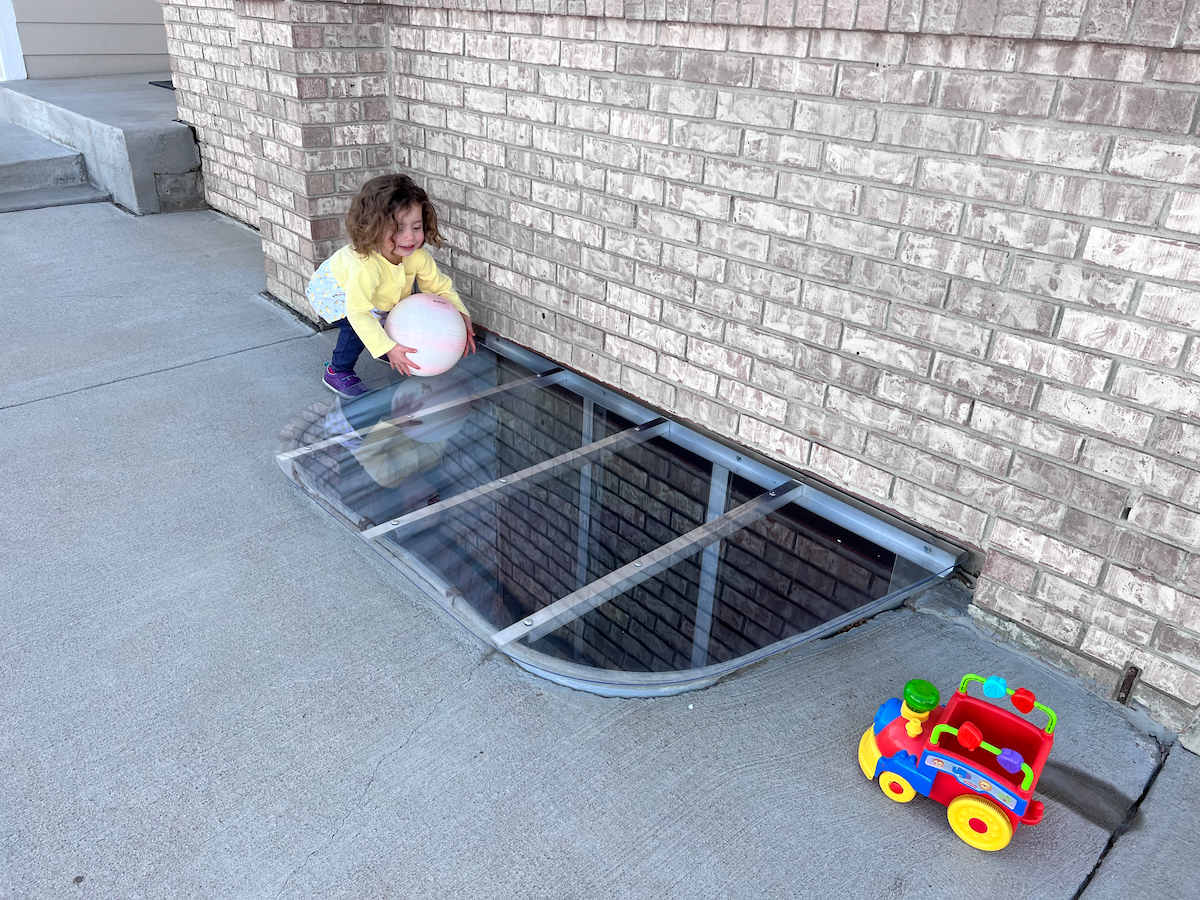 Child Grabbing Ball Beside Window Well Cover